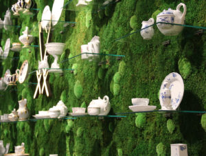 wall of green moss with glass shelves holding dishware and china