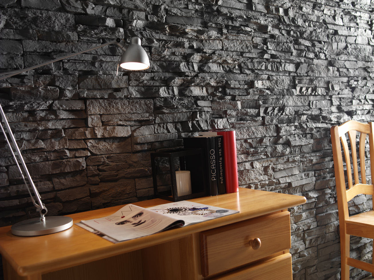 rock wall with wooden desk and chair against it with books and a silver lamp on the desk