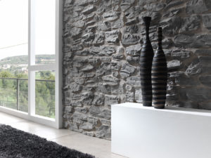 stone textured wall next to window whit white table in front of it with black bottles on the table